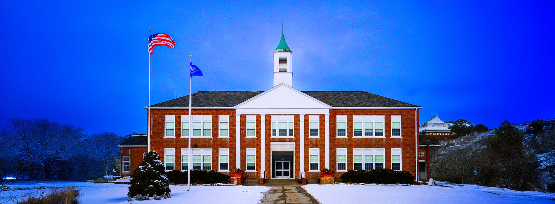 The image features a school building with a prominent clock tower, set against a snowy landscape under a clear blue sky.