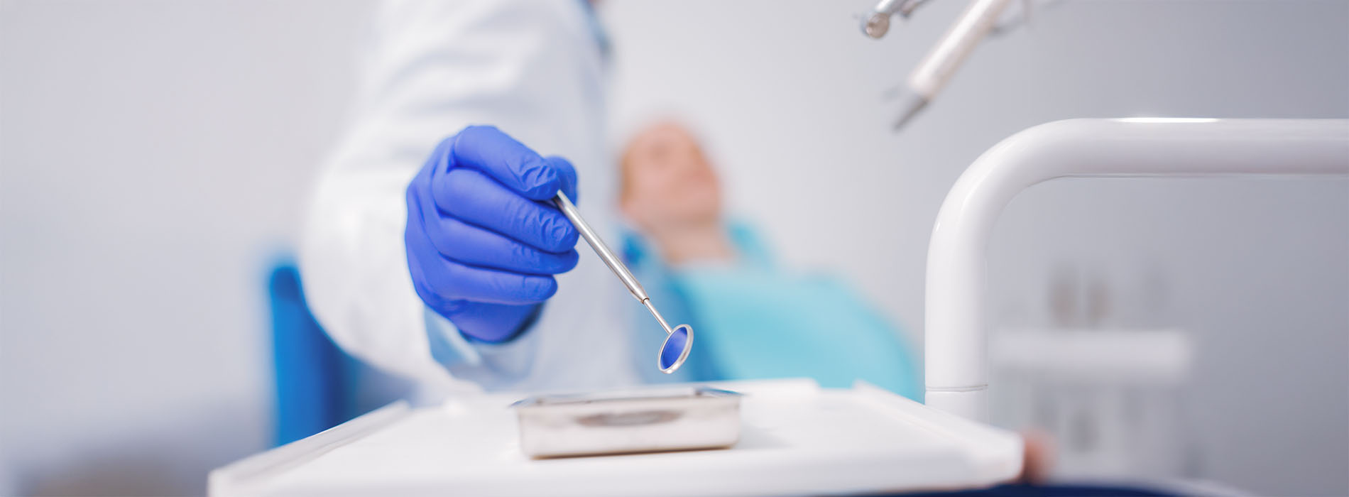 A dental professional wearing protective gloves and holding a dental mirror over a patient s mouth during an examination.