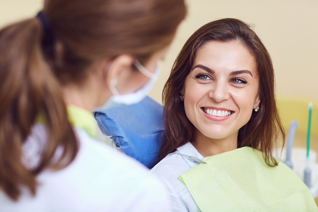 A woman in a dental chair receiving dental treatment from a smiling female dentist.