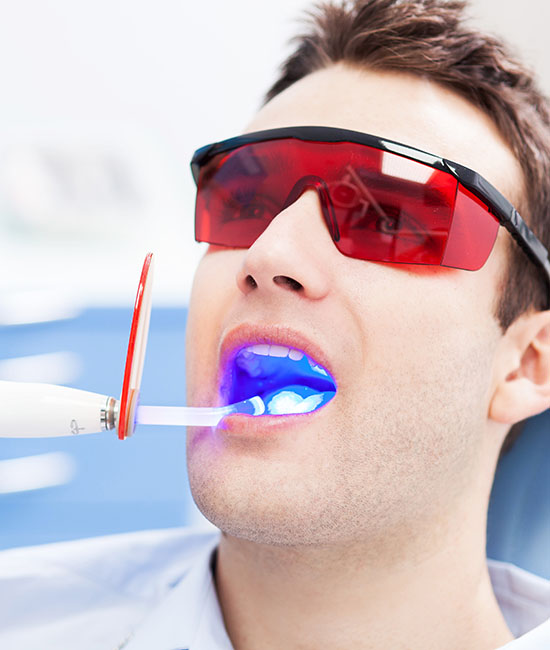 A man wearing red goggles is using an electric toothbrush on himself with a blue light effect.