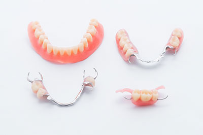 The image shows three pairs of dentures displayed against a white background, with each pair exhibiting different levels of wear and coloration, suggesting various stages of dental decay or replacement.