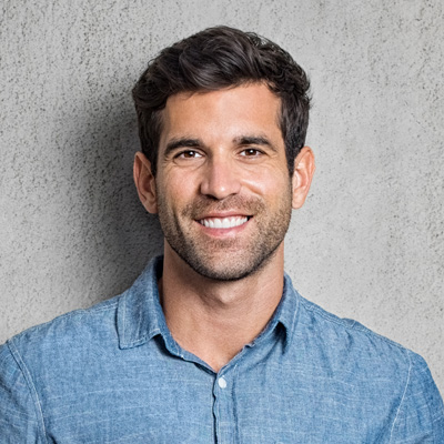 A man with a beard smiles at the camera against a grey background.