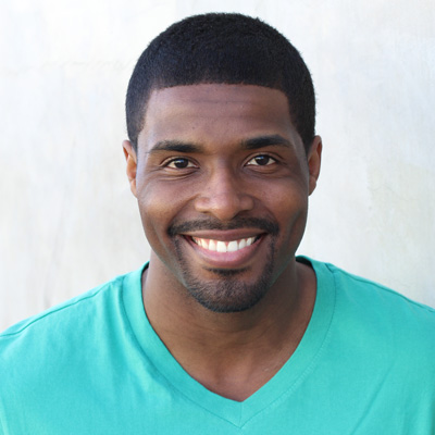 An elderly couple embracing and smiling at the camera outdoors during the daytime.
