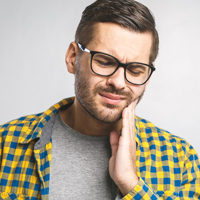 A man with glasses and a beard, wearing a yellow plaid shirt, is seen holding his chin and looking upwards with an expression of concern or worry.