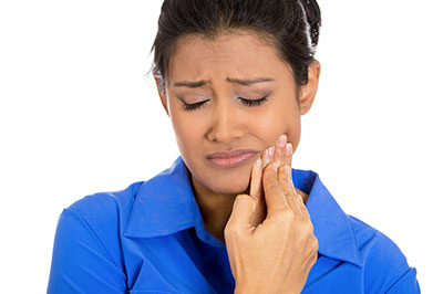 A woman with a concerned expression, holding her hand to her mouth, possibly in pain or discomfort, with a blue background.