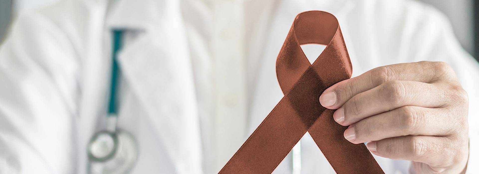 The image shows a person wearing medical attire holding a red ribbon with a white cross symbolizing cancer awareness.