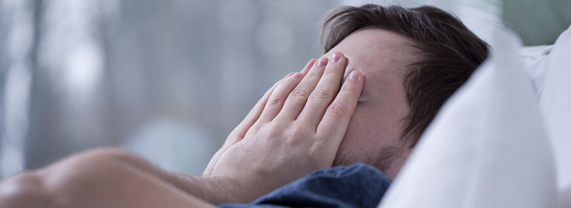 A person lying in bed with their face partially covered by their hand, appearing distressed or upset.