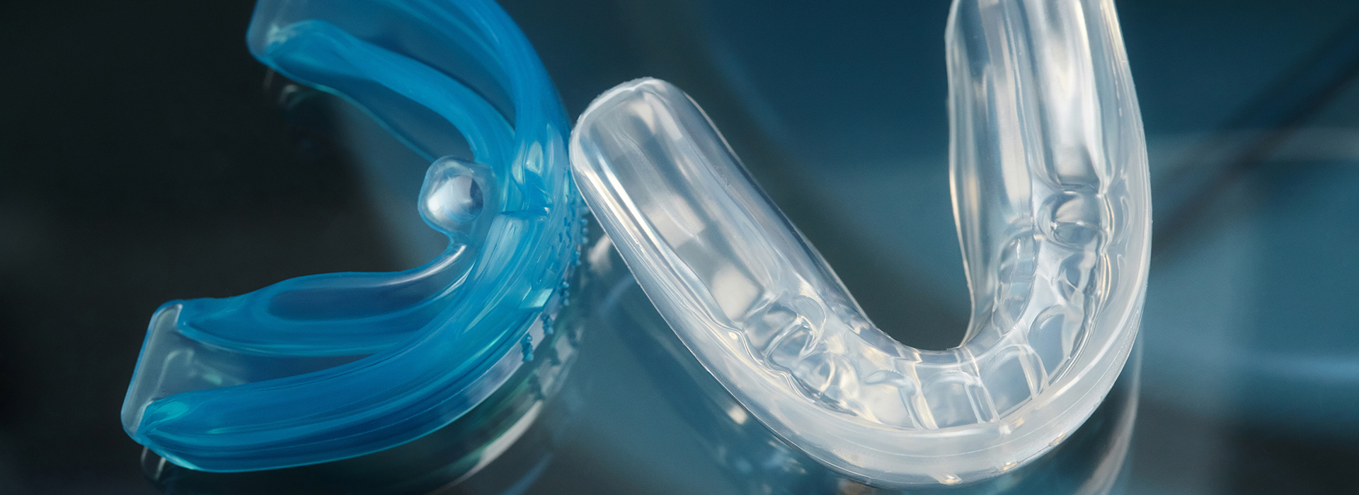 The image shows a close-up view of a clear plastic toothbrush with blue bristles against a blurred background, which appears to be a surface with a reflective quality.