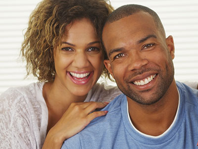 A man and woman are smiling at the camera, posing closely together for a portrait-style photograph.