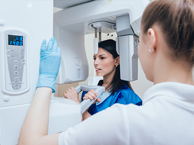 A woman in a blue jacket looking into a large white machine with a digital display, while another person, possibly a technician, stands beside her, observing the device.