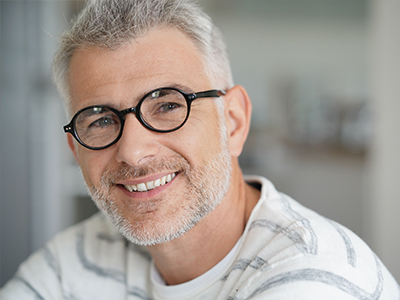 The image shows a middle-aged man with glasses smiling at the camera. He has graying hair and is wearing a light-colored shirt.