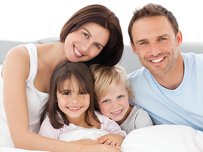 A family of four with two adults and two children posing on a bed for a portrait.