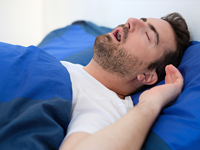 A person lying on a bed with their eyes closed and mouth open, appearing to be asleep or in a state of relaxation.