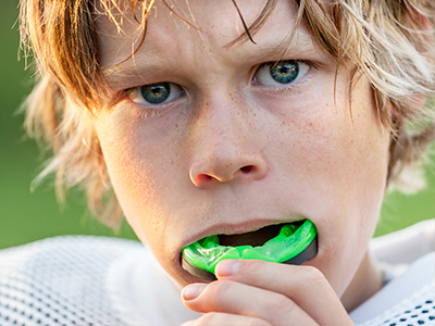 A young boy with blonde hair is seen brushing his teeth with a green toothbrush.