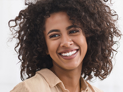 A smiling woman with curly hair and a joyful expression, wearing a brown top.